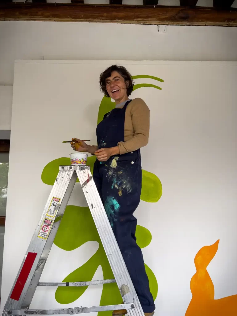 Artista sonriendo mientras pinta un mural abstracto en una escalera, usando diluyentes profesionales de El Paint Lab.