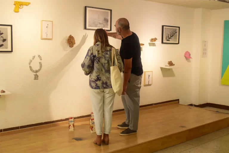 Dos personas observan obras de arte contemporáneo exhibidas en una galería durante una feria de arte, con piezas en la pared y objetos intervenidos en el suelo.